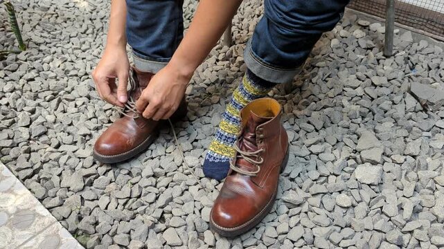 Man in jeans putting on and tying red leather boots shoes, in rock floor, rugged, stock video, 4K.