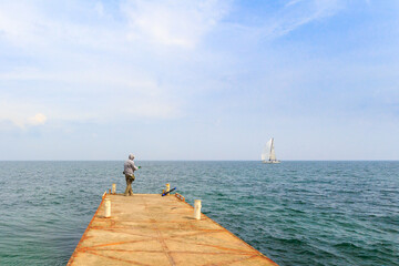 A fisherman catches fish on a pier on a clear sunny day. A man with a fishing rod on the seashore....