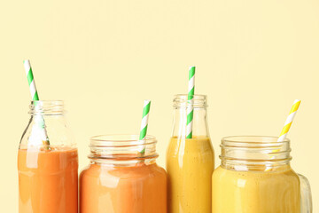 Glasses and bottles of different tasty smoothie with straws on yellow background