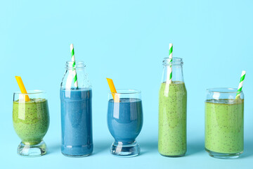 Glasses and bottles of different tasty smoothie with straws on blue background