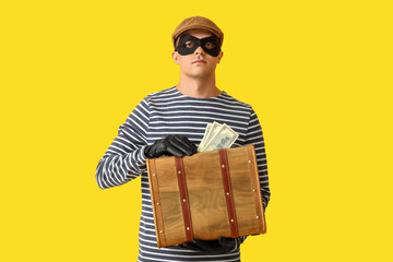 Male thief with briefcase of money on yellow background
