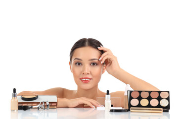 Young Asian woman with makeup products at table on white background, closeup