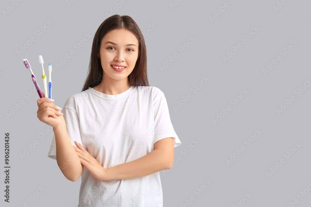 Sticker Young Asian woman with toothbrushes on grey background