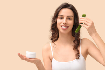 Beautiful young woman with aloe vera and jar of cream against beige background