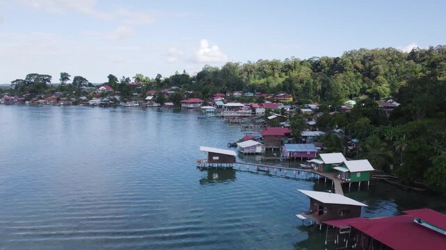 Aerial view of rustic homes along the coastline of Bastimentos Island in Panama. Homes on stilts with lush greenery in the background.