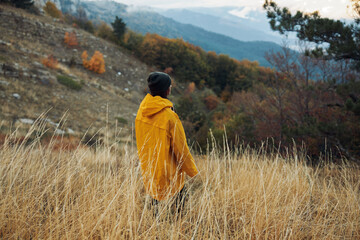 A solitary figure in a vibrant yellow coat standing amidst a picturesque field with majestic mountains in the background