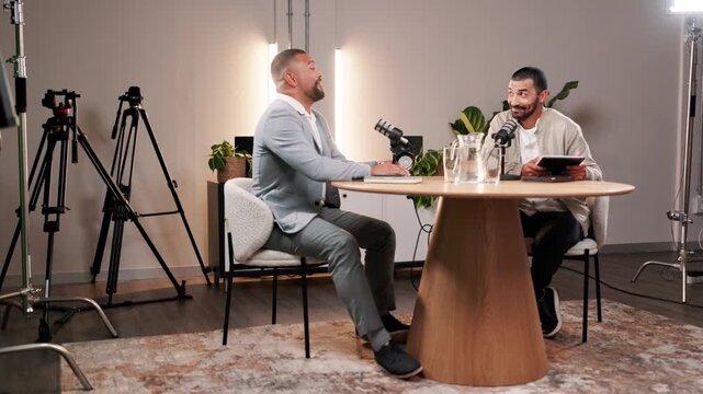 Talking, interview and podcast with guest on microphone for show, broadcast and laughing. Live streaming, radio host and men record audio for content creation and business tips with tablet in studio