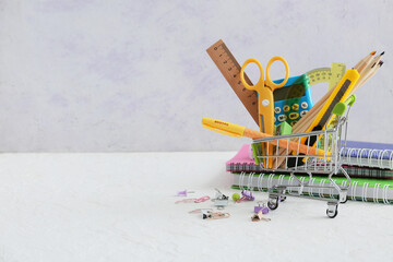 Tiny shopping cart with stationery on table against grey background