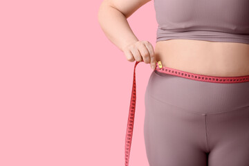 Overweight woman measuring waist on pink background, closeup. Diet concept