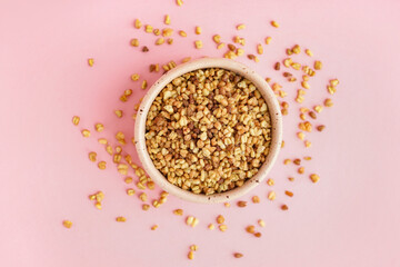 Bowl with raw buckwheat grains on pink background