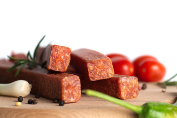 Savory spicy sausage sticks on wooden board, with garlic, herbs, tomatoes nearby.