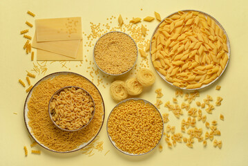 Bowls with different types of delicious uncooked pasta on beige background