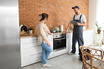 Male technician with woman near broken oven in kitchen