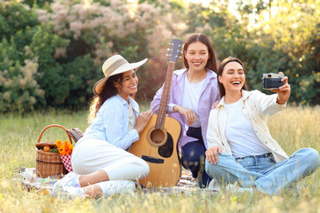 Female friends with guitar taking selfie on picnic in park