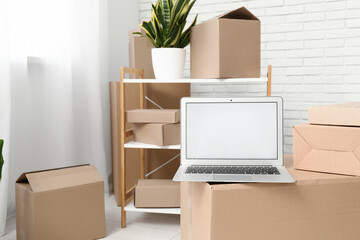 Blank laptop with moving boxes in light room, closeup