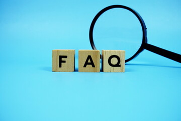 FAQ with wooden blocks alphabet letters and Magnifying glass on blue background