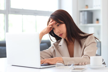 Obraz premium Tired Asian businesswoman working with laptop at table in office