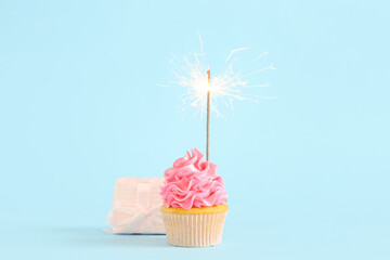 Sweet Birthday cupcake with sparkler and gift box on blue background