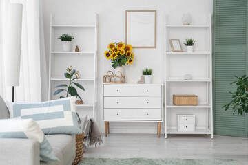 Interior of light living room with shelf units, drawers and sunflowers in vase