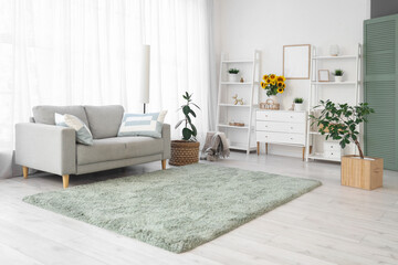 Interior of light living room with sofa, shelf units and sunflowers in vase