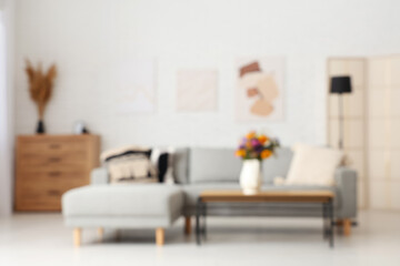 Comfortable sofa and vase with wild flowers on coffee table in living room. Blurred view