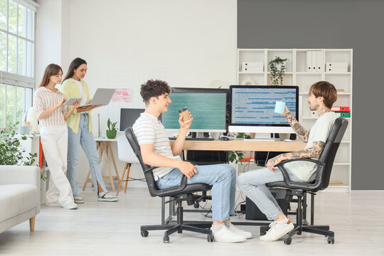 Male programmers with cups of coffee working at table in office