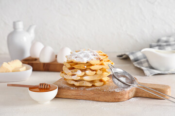 Delicious Belgian waffles with powdered sugar and honey on board on table against white background