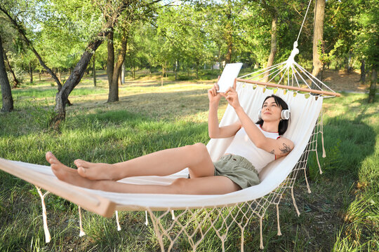 Young woman with headphones and tablet computer resting in hammock outdoors