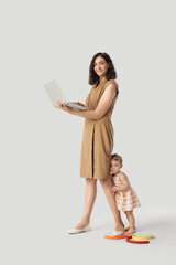 Fototapeta premium Working mother with laptop and her little baby on light background