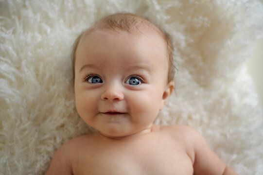 Portrait of beautiful baby big blue eyes smiling on white rug