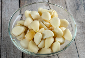 high angle shot of a glass bowl of garlic on wooden table