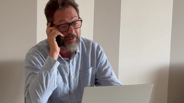 Busy mature man office worker manager consulting client by telephone checking information on laptop screen. Professional teleworker broker salesman offer goods services remotely using phone laptop