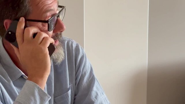 Smiling business man using laptop talking on cell phone sits at desk. Happy confident male professional manager web designer consulting client about online project making business call at workplace.