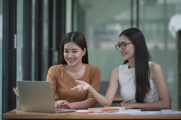 Two young Asian businesswomen discussed investment project work and planning strategy. Business people talk together on laptop computers at the office.