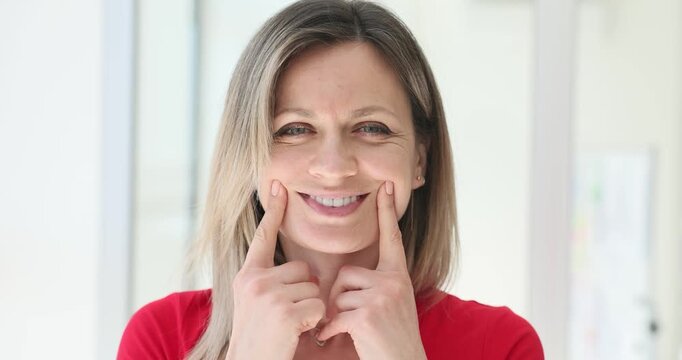 Woman pretends happiness by lifting lips with fingers. Lady demonstrates struggle to hide depression behind seemingly pleased expression
