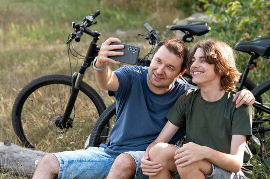 Father and his teenager son taking selfie on mobile phone while walking and cycling in nature