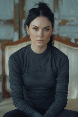 Fototapeta premium adult woman sitting on armchair with serious look, looking at camera, portrait, vertical, gray, cold,