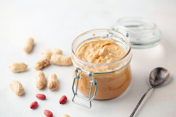 Peanut butter or paste jar and heap of nuts on light background.