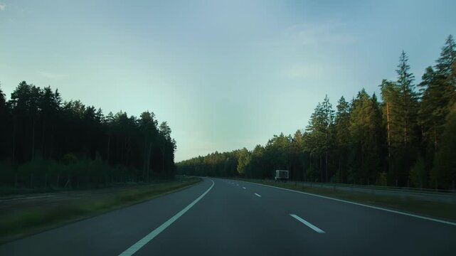 View through rear windshield windscreen of car in motion, back glass screen. Dual carriageway with two-lane road along forest. Countryside roadway out of town. Travel journey. Traffic crash barrier