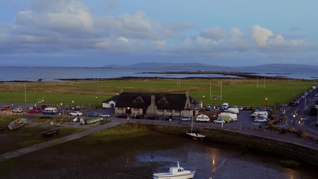 Colorful aerial dolly shot of Claddagh Park's green lawns, Galway Bay, and the Burren in the background at twilight