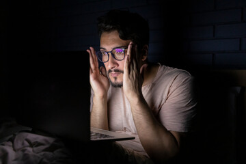 Worried man working on laptop in bed at night