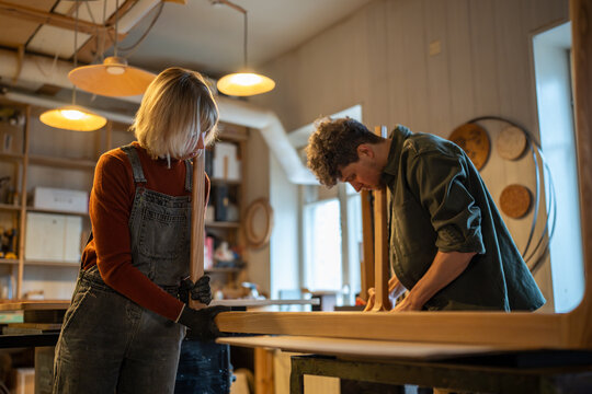 Carpentry workshop. Focused spouses woman man working in carpentry workshop assembling table, joining base and legs. Working together on an individual order. Furniture manufacturing, small business