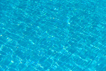 Swimming pool with turquoise blue clear water. Reflections of sky on a sunny day. Waves, reflections and light refraction create abstract shapes. Abstract vacation background vibrant cyan tones.