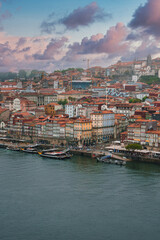 Colorful historic buildings with red-tiled roofs line the bustling waterfront of Porto's Ribeira district, featuring boats, a church spire, and dramatic clouds.