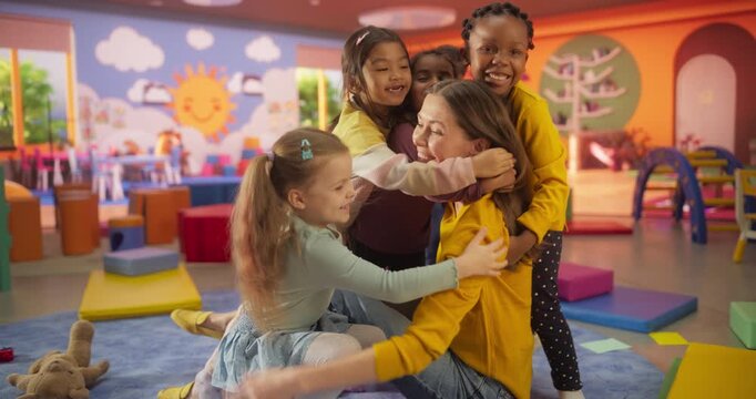 Portrait of an Attractive Happy Young Teacher Hugging with Young Cute Kids in a Modern Colorful Kindergarten Room. Female Educator Taking Care of Happy Active Multiethnic Children in Daycare