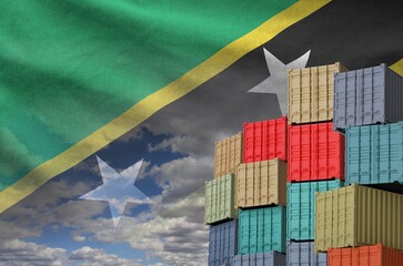 Saint Kitts and Nevis flag and big stack of shipping cargo containers in docks with sky background...