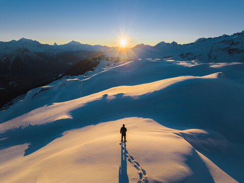 Lone traveler trekking through snowy Swiss Alps at sunset