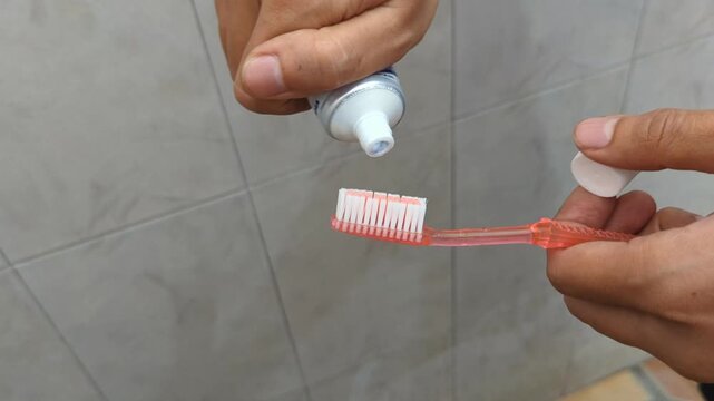 A man in the bathroom squeezes white toothpaste from a tube onto a red toothbrush on a bathroom, brushing her teeth, morning and evening procedures, hygiene, stock video, 4K.