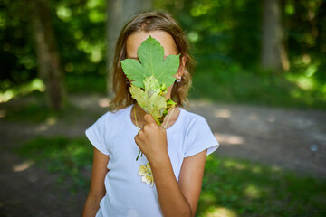 Young Girl Playfully Hiding Her Face With Leaves in Natural Forest Setting