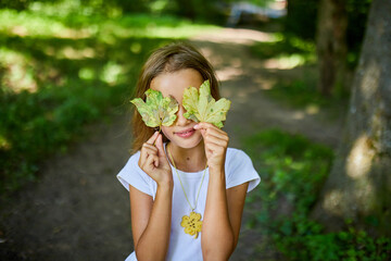 Young Girl Playfully Hiding Her Face With Leaves in Natural Forest Setting
